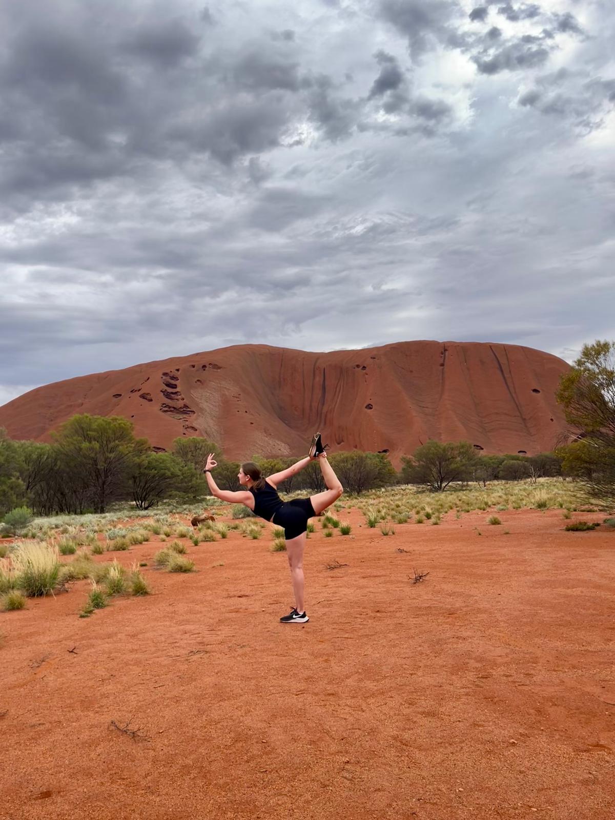 Carolina Neumayr in der Tänzer-Pose (Natarajasana) vor dem Uluru während ihrer Yoga-Ausbildung in Australien