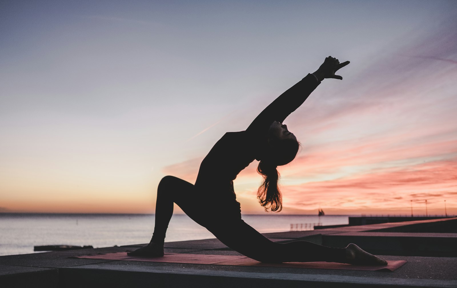 Vinyasa Yoga: fließende Haltung im Ausfallschritt mit gestrecktem Arm bei Sonnenuntergang